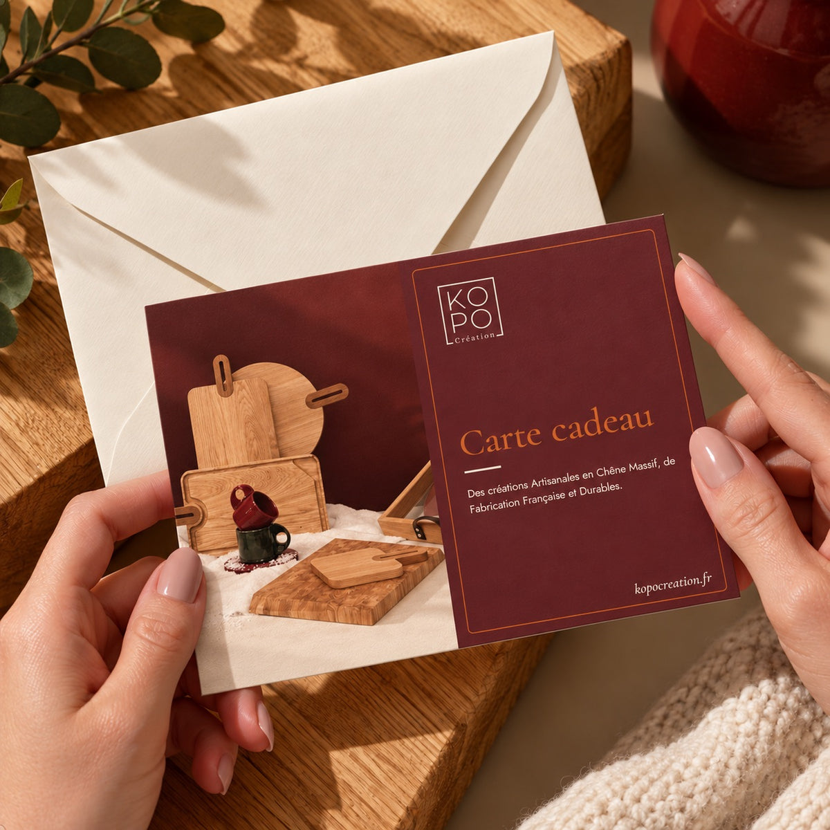 Carte cadeau Kopo Création tenue en main devant une enveloppe ivoire, idée cadeau en chêne massif fabriqué en France