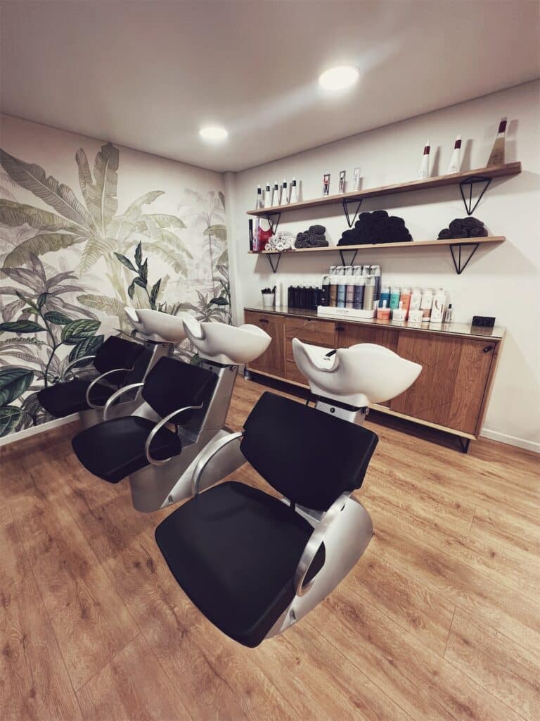 Espace de coiffure moderne avec deux fauteuils de lavage noirs et argentés sur sol en bois clair, aménagement sur mesure signé Kopocreation ébénisterie